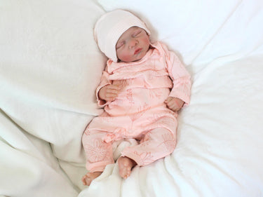 A baby doll positioned on a patterned blanket, emphasizing its cute appearance and soft texture.